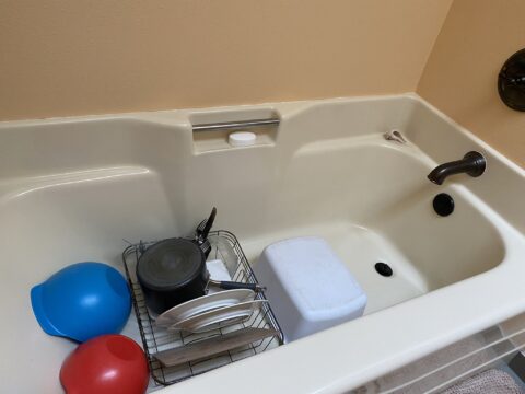 what to expect during construction shows a bathtub with dishes drying on a drying rack as a make shift kitchen