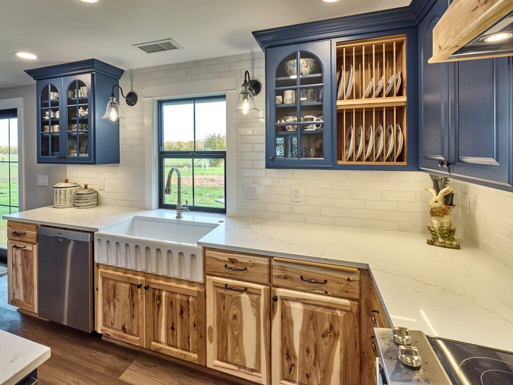 Knotty hickory custom cabinetry, blue painted upper cabinets, large white farmhouse sink, garden window above sink with white quartz countertop and porcelain tile backsplash built by Henderer Design + Build in Corvallis Oregon