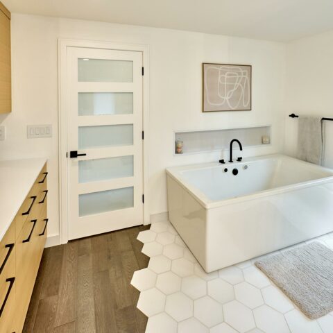 modern master suite remodel with white hex flooring tile to wood flooring transition, white oak custom cabinetry, and oversized tub