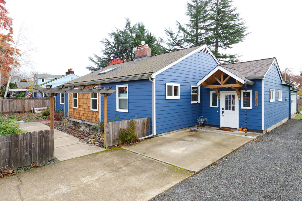 Single family residence exterior with cedar shingle siding and blue paint, wood fence and white entry with trusses, sky and trees in background built by Henderer Design + Build Corvallis, Oregon