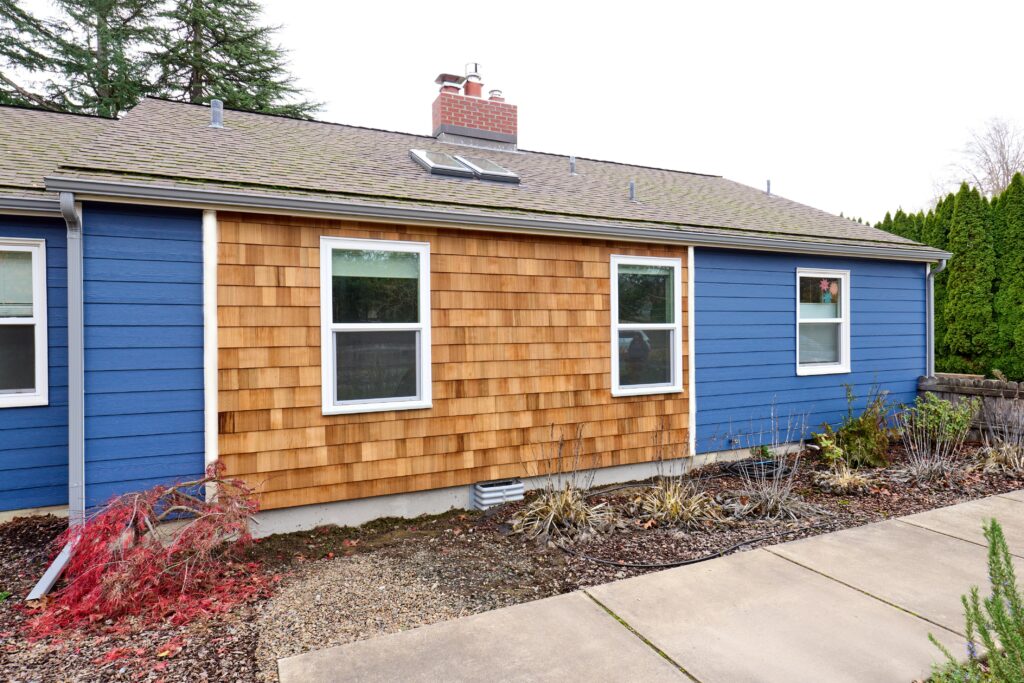 Single family residence exterior with cedar shingle siding and blue paint, wood fence and white entry with trusses, sky and trees in background built by Henderer Design + Build Corvallis, Oregon